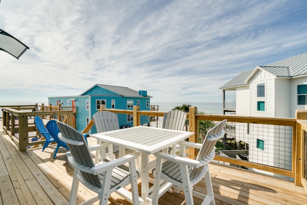 wooden deck patio with gray table and four chairs surrounding it with beach view in cape san blas