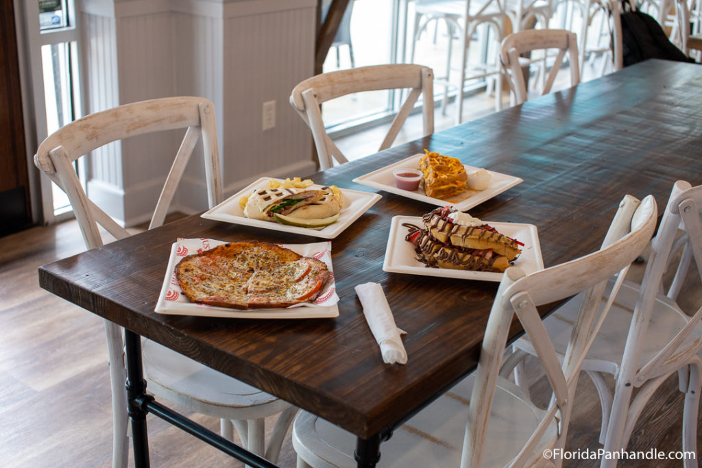 a plate of extra thin crust pizza next to a plate of waffles with strawberries, whipped cream and chocolate drizzle at Just Love Coffee Cafe in Destin, Florida