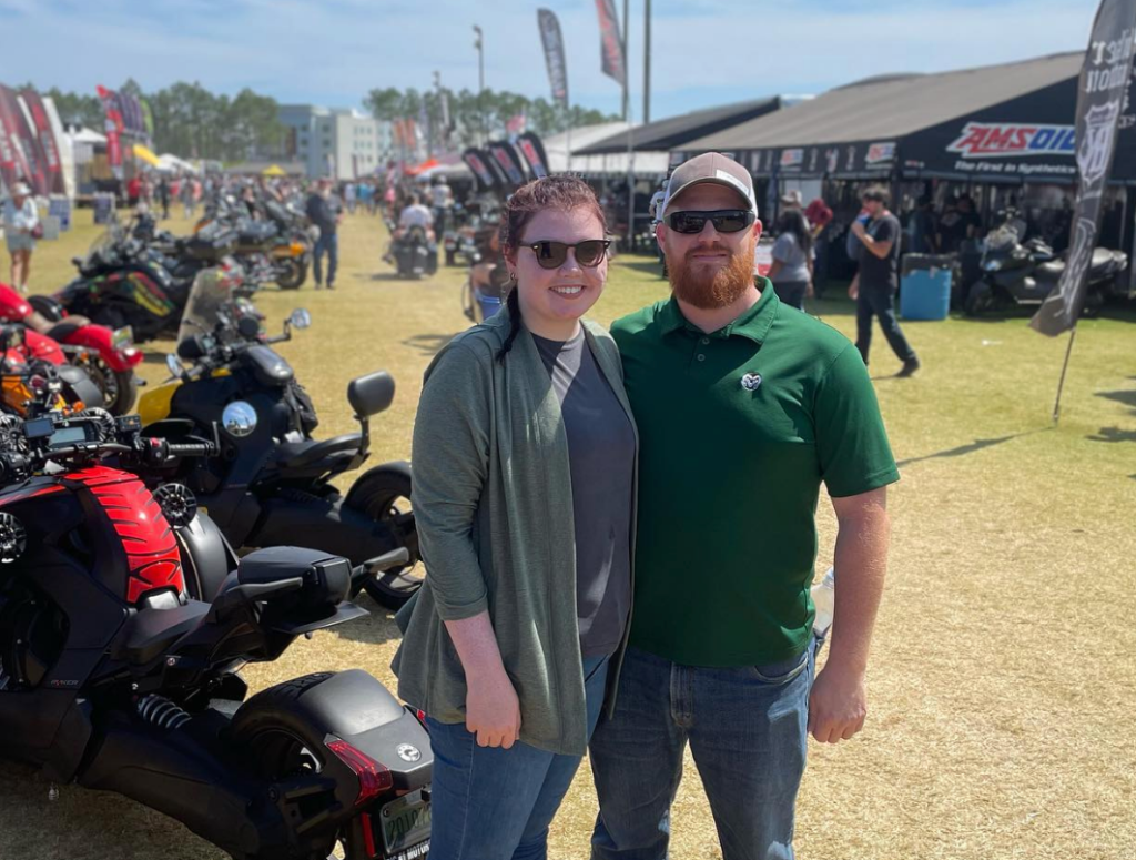 man and women smiling and posing for picture next to a line of motorcycles 