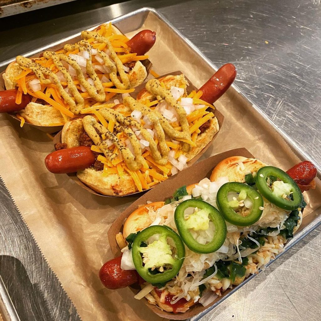 three loaded hot dogs with cheese, mustard, and jalapeños on top