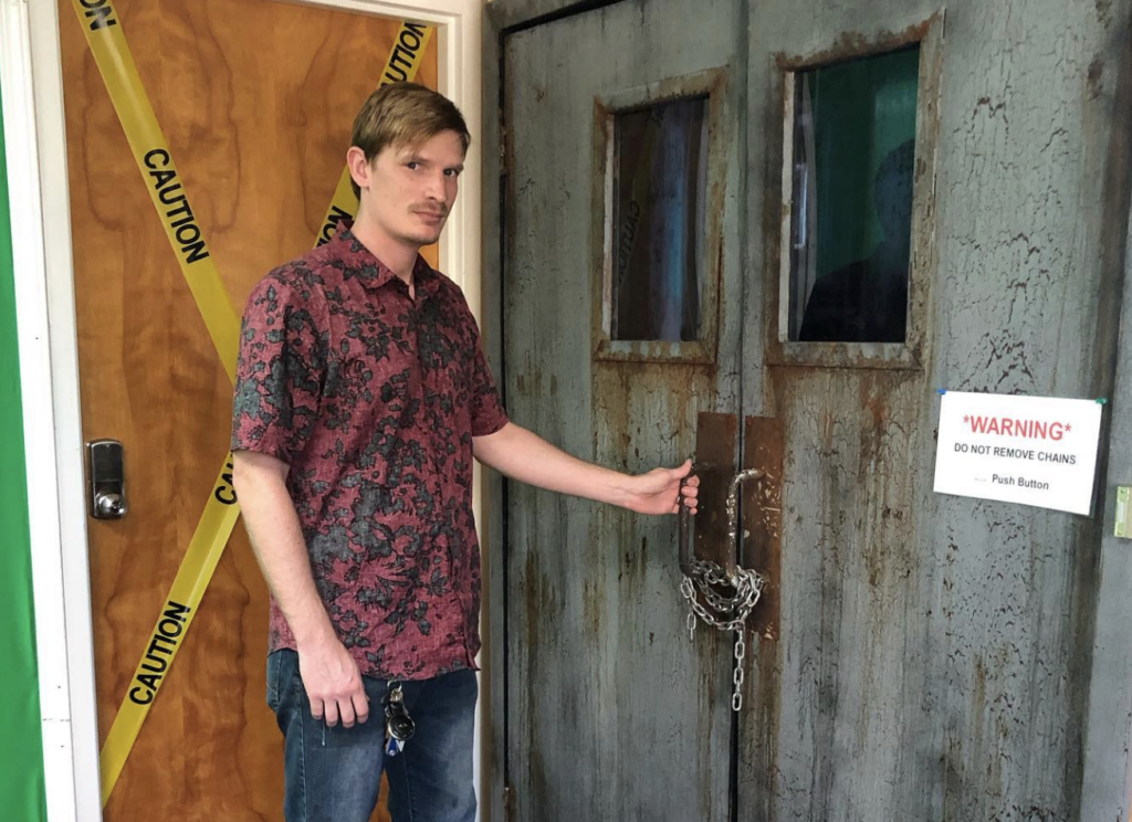 guy holding door with caution tape on the door in an escape room 